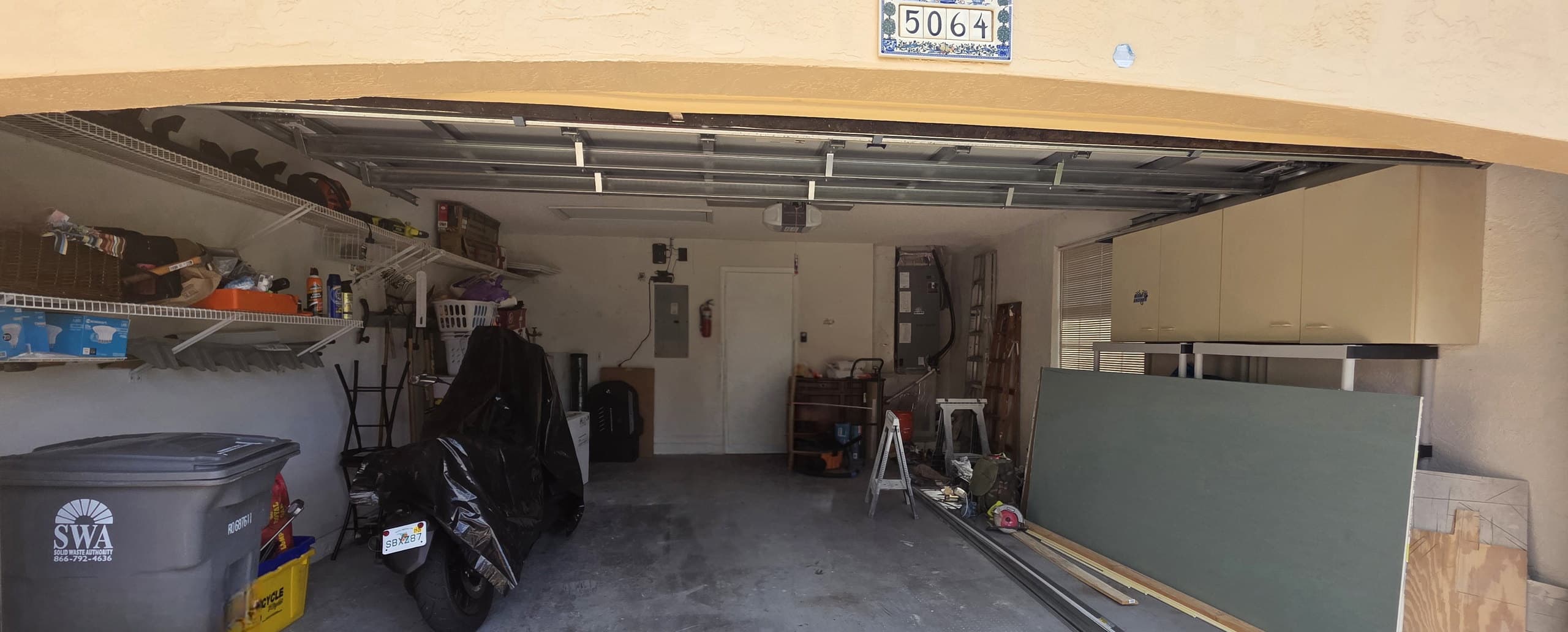 Uncoated residential garage slab with stored items and a covered motorcycle, photographed from the driveway.